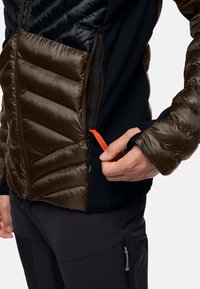 Giacca isolante con dettagli trapuntati marroni e tessuto elasticizzato nero. Presenta un tirazip arancione e un design elegante. Fit aderente in vita.