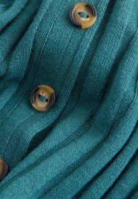 Maglione lavorato a maglia color verde-teal con texture a coste, caratterizzato da grandi bottoni rotondi marroni lucidi come dettagli. Materiale morbido con un aspetto accogliente.