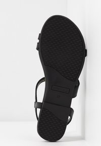 Semelle de sandale plate noire avec un motif de semelle ondulé, bride de cheville, taille 37, et nom de la marque "ANNA FIELD" visible au dos.