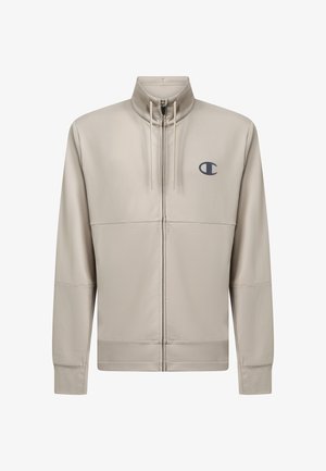 Chaqueta beige claro con cremallera, cuello alzado, cordones, mangas largas y un pequeño logo oscuro en el pecho izquierdo.