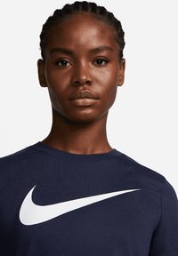 Námorně modré tričko s žebrovanou strukturou, na přední straně s velkým bílým logem Nike swoosh. Kulatý výstřih, krátké rukávy.