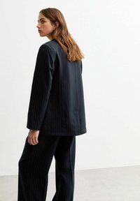 Giacca in tessuto a righe blu navy e pantaloni larghi coordinati. Tessuto liscio, taglio sartoriale e vestibilità rilassata. Design minimalista con linee pulite.
