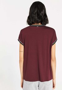 Burgundy short-sleeve top with black trim at the neckline and sleeves, featuring a relaxed fit and soft, smooth texture.