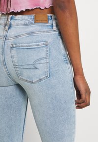 Lyse blå denimbukser med en tettsittende design, med et lærmerke på linningen og en baklomme med subtile sy detaljer.