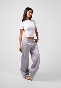Kuttet hvit t-skjorte med rosa tekst, kombinert med løstsittende grå sweatpants med elastisk liv og lommer.