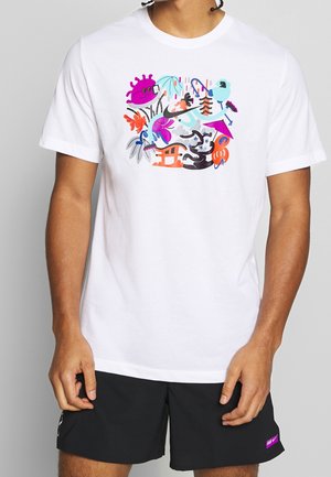 T-shirt blanc avec un design abstrait coloré comportant des formes violettes, orange et bleues ressemblant à des plantes, des animaux et des formes ludiques sur la poitrine.