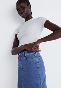 Pelēka pieguļoša T-kreklu ar īsām piedurknēm, apvienota ar vidēja garuma zilu džinsu svārku ar pogu priekšpusi un kabatām.