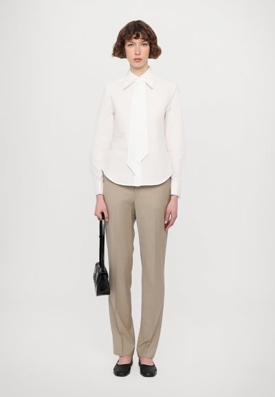 Camicia bianca con colletto, cravatta, pantaloni beige e ballerine nere, abbinati a una borsa nera. Tessuto morbido e vestibilità sartoriale.