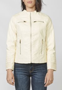 Giacca in finta pelle color crema con colletto rialzato, tasche con zip e dettagli ricamati intricati sulle maniche e sullo yoke.