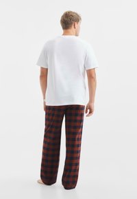 Witte katoenen t-shirt met korte mouwen, gecombineerd met geruite flanellen broek in donkerblauw en roestkleuren, met een losse pasvorm en rechte pijpen.