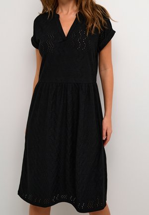 Vestido negro con mangas cortas enrolladas, un escote en V y un patrón texturizado. Presenta una falda acampanada y detalles bordados cerca del dobladillo.