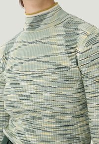 Pitkähihaista turtleneck-paitaa ribbineulosta. Ominaisuuksina vaaleanvihreä väri, jossa on keltaisia ja tummanharmaita vaakasuoria raitoja. Pehmeä rakenne ja istuva muotoilu.