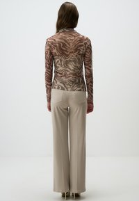 Top en voile à manches longues avec un motif zèbre marron et beige, associé à un pantalon large crème ; tissu lisse et coupe droite.