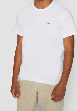 Hvid bomulds t-shirt med korte ærmer, rund halsudskæring, der har et lille horisontalt logo i rød, blå og hvid på venstre bryst.