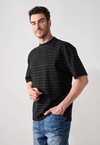 Sort kortærmet t-shirt med et stripet mønster i hvidt. Runde halsudskæring, afslappet pasform og blødt stof. Sammen med lyseblå jeans.