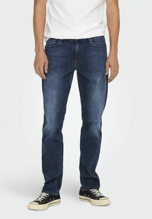 Jeans de mezclilla azul oscuro con un corte recto, que presentan un diseño de cinco bolsillos y detalles de desgaste sutil, combinados con zapatillas negras.
