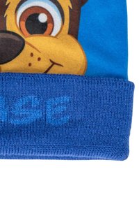 Beanie blu lavorato a maglia con un design di una faccia di cane cartone animato. Il risvolto è di un blu più scuro con lettering in rilievo. Tessuto morbido e testurizzato.