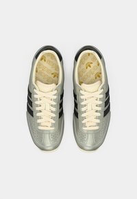 Szare i czarne sneakersy z perforowanym wzorem, kremowymi sznurowadłami i złotym logo na wkładce. Okrągły przód i gumowa podeszwa.