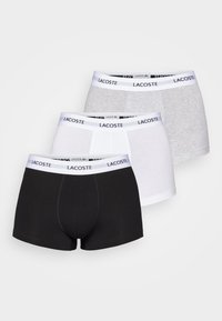 Drei Paare Lacoste Boxershorts: schwarz, weiß und grau. Jedes Paar hat einen kontrastierenden, gebrandeten elastischen Bund und eine enge Passform.