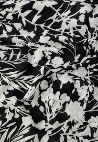 Sort-hvitt stoff med abstrakte blomster- og bladmønstre, som viser tekstur og lette folder i materialet.