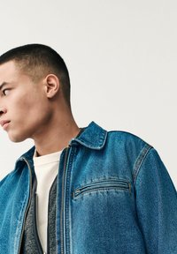 Chaqueta de denim en azul brillante, con cierre de cremallera, un bolsillo en el pecho con una cremallera sutil y un diseño clásico de cuello.