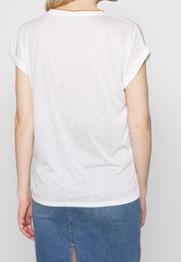 Hvid kortærmet T-shirt med en let glans, der har en rullet ærmekant og en orange accent ved udskæringen. Båret med en denimnederdel.