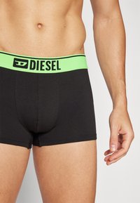 Μαύρα βαμβακερά μποξεράκια με φαρδύ νεον πράσινο λάστιχο που φέρει το λογότυπο "DIESEL". Λείο ύφασμα και εφαρμοστό σχέδιο.