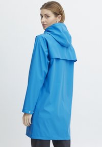 Waterdichte blauwe regenjas met capuchon, met een losse fit, lange mouwen, drukknoopmanchetten en een flapdetail aan de achterkant. Gladde textuur.