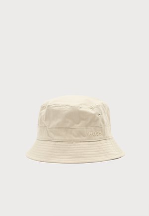 Béžový látkový klobúk bucket s prešitými detailmi a malým logom "BOSS" na boku, na jednoduchom svetlom pozadí.