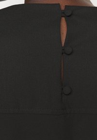 Back neck of a black garment with three fabric-covered buttons fastening a small keyhole opening on dark skin.