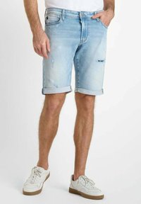 Pantalones cortos de mezclilla azul claro con puños doblados, que presentan un diseño desgastado y detalles desgastados. Combinados con zapatillas blancas.