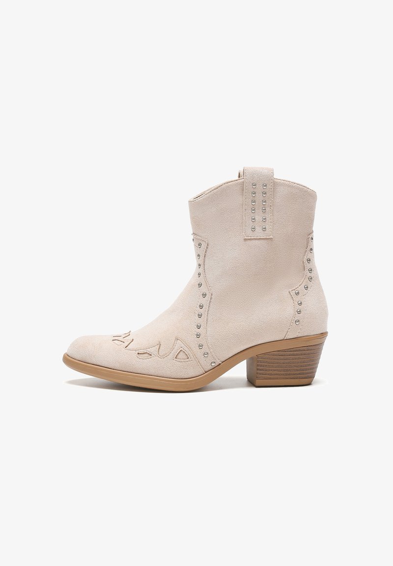 Botín de tobillo beige en suave ante con tachuelas plateadas a lo largo de las costuras y un diseño cosido en la puntera. Presenta un tacón apilado.