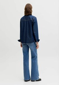 Denimist särk lõdva lõikega, tumesinist värvi ja nööbitavate varrukaotstega. Sobitatud helesiniste lõhenevate teksade ja mustade pahkluu saabastega.