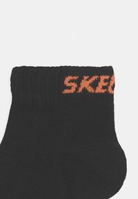 Black sock featuring a ribbed cuff and orange "SKECHERS" logo knitted into the top. Soft texture, ankle length design.