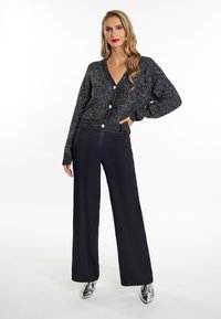 Cardigan lungo a maniche lunghe nero e argento con scollatura a V, grandi bottoni e un motivo testurizzato, abbinato a pantaloni neri a gamba larga e tacchi metallici.