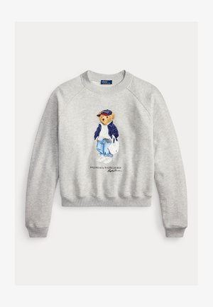Felpa grigio chiaro con grafica di un orso che indossa una giacca blu navy, maglione bianco, jeans, sneakers, cappellino e porta una borsa bianca.