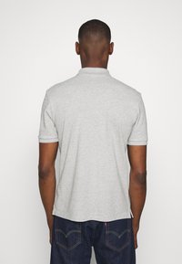 Harmaa lyhythihainen polo-paita, jossa on kaulus, valmistettu pehmeästä kankaasta, suora leikkaus ja resorit hihansuissa. Yhdistetty tummiin farkkuihin.