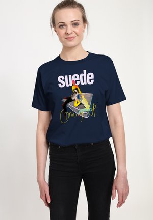 T-shirt navy avec un texte "suede" et un design graphique comportant une figure colorée, associé à un jean noir et à un col rond basique.