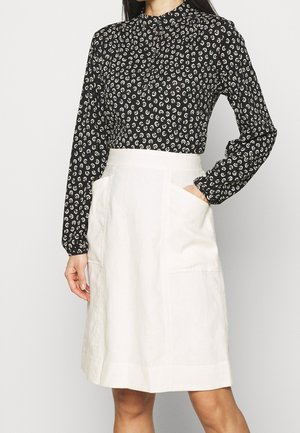 Blouse noire avec un motif paisley blanc, col montant et manches longues. Jupe en lin beige clair avec deux poches avant et coupe droite.