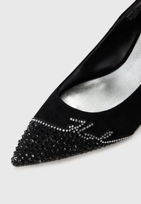 Black suede high-heeled shoe with pointed toe, embellished with black rhinestones and silver accents along the upper edge. Silver lining inside.