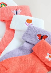 Fire farverige strikkede sokker med broderede motiver af sommerfugle, en blomst og en tulipan på manchetterne, lagt overlappende.