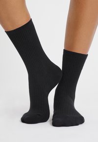 Calze nere a coste con design a metà polpaccio, caratterizzate da una texture morbida e punta senza cuciture per il massimo comfort. Adatte per un abbigliamento casual o per l'uso quotidiano.