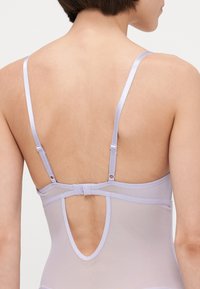 Lila bodysuit z drobnimi nastavljivimi naramnicami, nizkim hrbtom in varnim zapiranjem. Prosojen material z gladko teksturo in čistimi linijami.