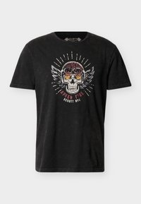 T-shirt noir à manches courtes avec un graphisme d'un crâne enflammé portant un casque avec des ailes et le texte "Motorcycle Speed Fire Schott NYC."