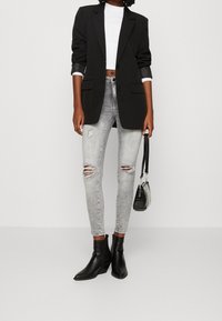 Černý oversized blejzr, bílý crop top, potrhané světle šedé úzké džíny, černé kotníkové boty a malá černá kabelka.