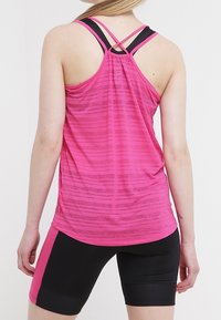 Růžový sportovní tílko s texturovaným pruhovaným vzorem, s designem racerback a kontrastními černými ramínky. Černé přiléhavé šortky.