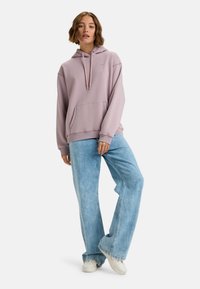Lila hoodie med en framficka, dragsko för huva och ribbade muddar. Kombinerad med ljusblå vida jeans och vita sneakers.