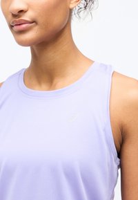 Γυναίκα που φοράει αμάνικο αθλητικό τοπ ανοιχτό μωβ με μικρό λογότυπο στο στήθος, εμφανιζόμενη από το λαιμό έως τον άνω κορμό με φόντο λευκό.