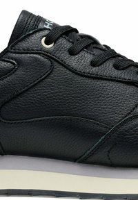 Zapatilla de cuero negra con material texturizado, costuras tonales y cordones redondos. Suela de goma de color claro con una sutil marca en la lengüeta.