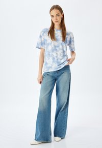 Camiseta de tie-dye azul claro con mangas cortas y un estampado gráfico en el pecho, combinada con jeans de mezclilla azul de pierna ancha.